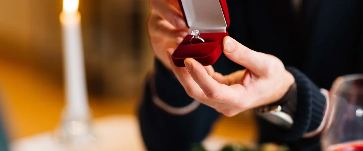 Young man showing his girlfriend red velvet box with engagement ring